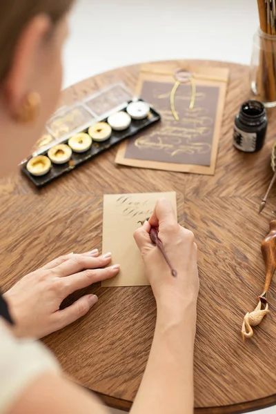 Attraktiv kvinna kalligraf håller en penna med bläck och undertecknar ett kort i handskrivet typsnitt. Närbild. Mjukt fokus. — Stockfoto