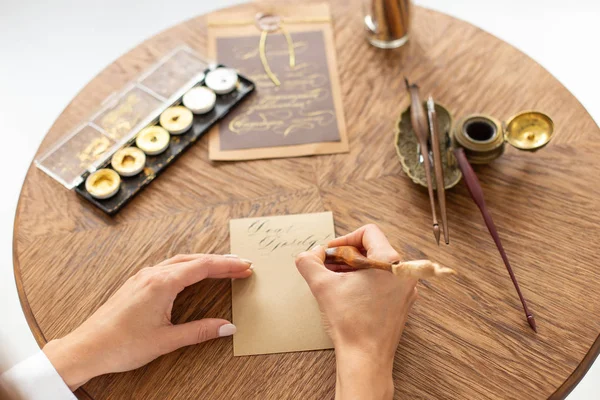 Calligrapher is holding a pen with ink. The girl writes a letter in handwritten font. Creative workshop of the artist. Soft focus. — Stock Photo, Image