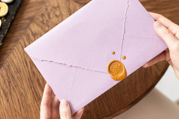 A woman is holding a welcome envelope with a wax seal, a gift certificate, a postcard, a wedding invitation. Soft focus. Close-up.