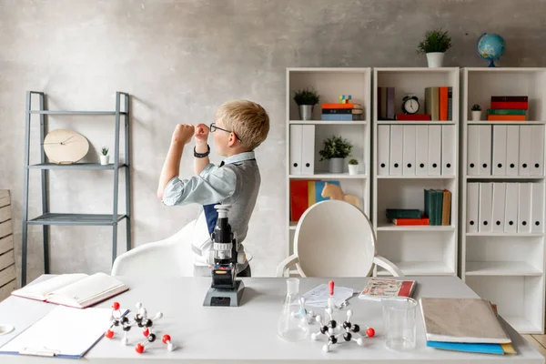 A szemüveges iskolás fiú az üvegen lévő mintát nézi kémiaórán. — Stock Fotó