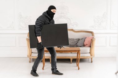 Hırsız sıva ile lüks dairede bir suç işler. Siyah balaclava ile Hırsız modern pahalı televizyon çalmak.