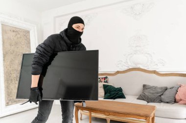 Adam hırsız evden televizyon çalıyor. Siyah balaclava ile hırsız modern pahalı televizyon çalmak. Sıvalı lüks daire.