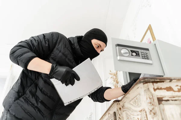 A tolvaj kinyitja az elektronikus széfet. A betörő vállalja a bűncselekmény luxus apartman stukkó. Tolvaj fekete Balaclava lopás Safe Box. — Stock Fotó