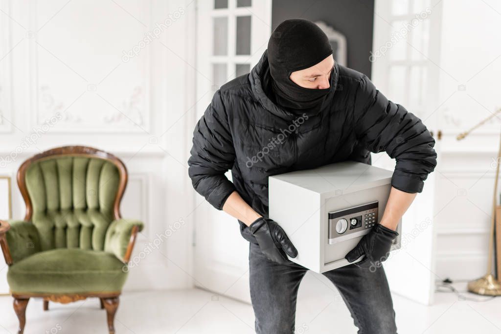 Thief with black balaclava stealing modern Electronic safe box. The burglar commits a crime in Luxury apartment with stucco.