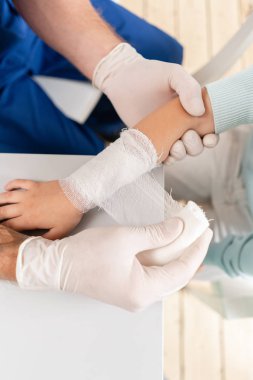 Mavi üniformalı doktor, kolunda travma olan bir erkek elinin etrafına elastik bandaj yapar. hastanede