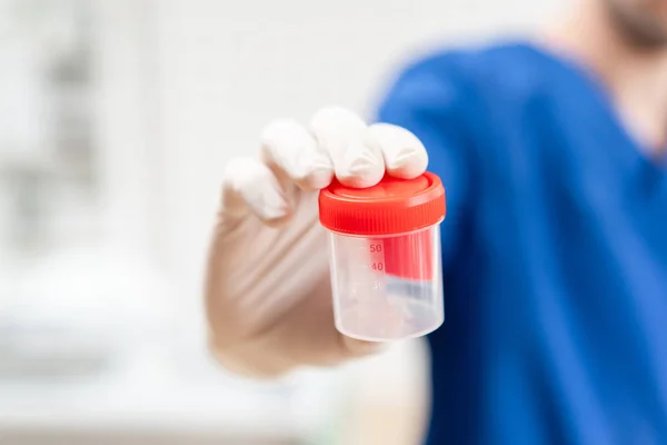 mavi üniforma ve lateks eldiven doktor idrar örnekleri, hafif arka plan almak için boş bir plastik konteyner tutuyor. Tıbbi konsept.