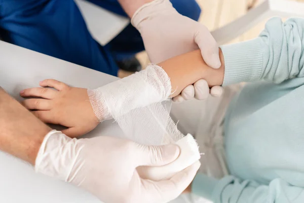 Doctor in blauw uniform maken elastische verbonden rond een jongen hand met trauma in zijn arm. — Stockfoto