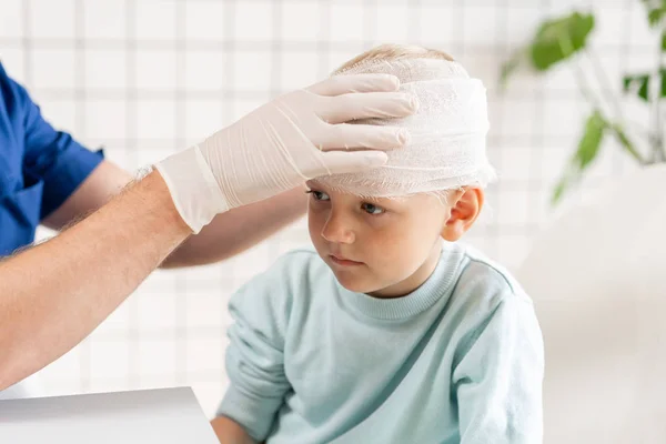 Doktor obtloul chlapečka s traumatem v hlavě a elastickou bandovici kolem hlavy — Stock fotografie