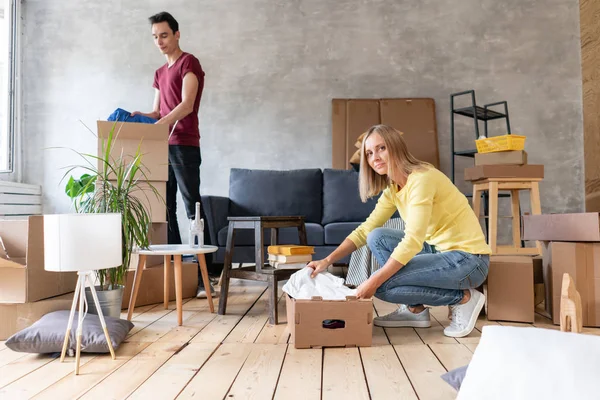 Feliz casal sorrindo se movendo em uma nova casa e desempacotando caixas de papelão, relocação e conceito de renovação — Fotografia de Stock