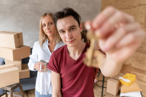 Junges glückliches Paar, das sich umarmt und Schlüssel zum neuen Haus zeigt. glückliche Familie, die zusammen in eine neue Wohnung zieht. Umzugskonzept — Stockfoto