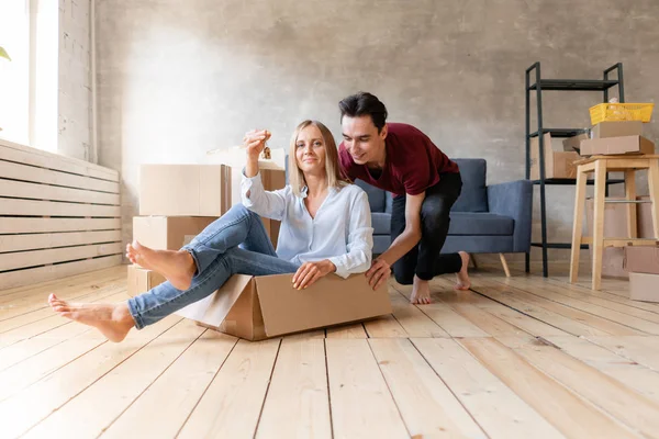 Glückliches Paar, das Spaß hat und im neuen Zuhause in Pappkartons reitet. junges Paar zieht gemeinsam in eine neue Wohnung. Umzugskonzept — Stockfoto