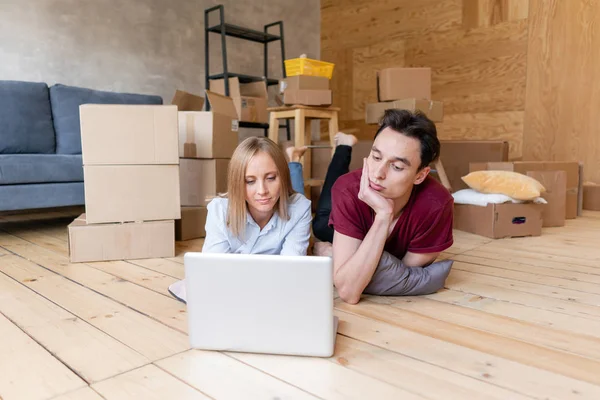 Glückliches Paar, das zusammen auf dem Boden liegt und beim Einzug ins neue Zuhause drahtloses Internet nutzt. Familie zieht gemeinsam in eine neue Wohnung. Umzugskonzept — Stockfoto