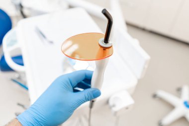 Diş polimerizasyonu lambası dişçi elinde, ultraviyole ışık ve lazerle. Dişçi kliniğindeki stomatolojik alet. Tıp, sağlık, stomatoloji kavramı.