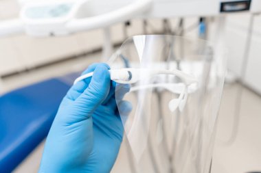 Diş hekiminin eldivenin yakın çekim eli diş koruyucu maskesi tutar. Diş hekiminin muayene yaptığı ve sonuçlandırdığı ofis.