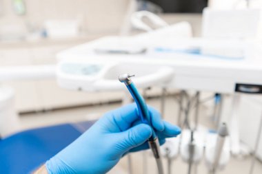 Eldivendeki dişçinin eli dişçi için yüksek hızda türbin taşıyor. Diş hekiminin teftiş yaptığı ve sonuca vardığı ofis..