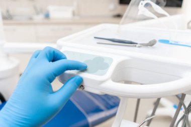 Eldivenli diş hekiminin eli sandalyenin kontrol düğmelerine basar... Klinikte diş işleri. Ameliyat, diş değiştirme. Tıp, sağlık, stomatoloji kavramı.