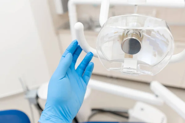 Крупним планом рука стоматолога в рукавичці налаштовує лампу. . . Управління, де стоматолог проводить огляд і завершує . — стокове фото