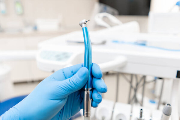 Close-up hand of dentist in the glove holds dental high speed turbine. Office where dentist conducts inspection and concludes.