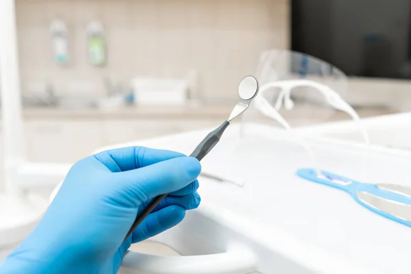 The hand of the dentist in the glove holds tool mirror. Stomatological instrument in the dentist clinic. Dental work in clinic. Office where dentist conducts inspection and concludes. — Stock Photo, Image