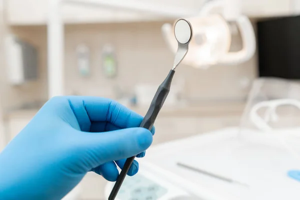 The hand of the dentist in the glove holds tool mirror. Stomatological instrument in the dentist clinic. Dental work in clinic. Office where dentist conducts inspection and concludes. — Stock Photo, Image