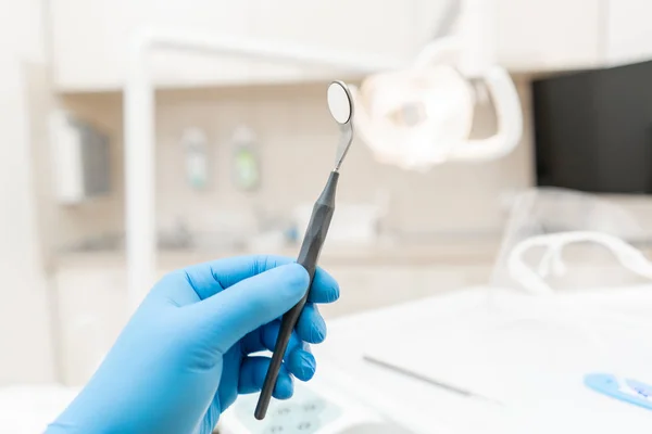 The hand of the dentist in the glove holds tool mirror. Stomatological instrument in the dentist clinic. Dental work in clinic. Office where dentist conducts inspection and concludes. — Stock Photo, Image