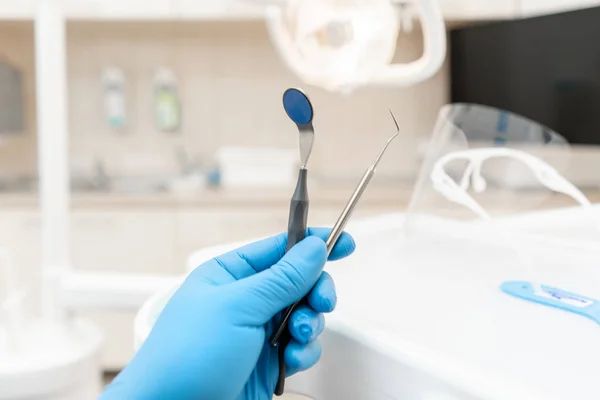 The hand of the dentist in the glove holds tool probe and mirror. . Stomatological instrument in the dentist clinic. Dental work in clinic. Office where dentist conducts inspection and concludes. — Stock Photo, Image