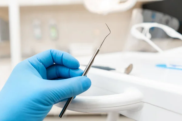 The hand of the dentist in the glove holds tool probe. . Stomatological instrument in the dentist clinic. Dental work in clinic. Office where dentist conducts inspection and concludes.