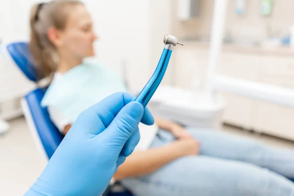 Primo piano mano del dentista nel guanto tiene turbina dentale ad alta velocità. Il paziente sulla sedia blu sullo sfondo. Studio in cui il dentista effettua l'ispezione e conclude . — Foto Stock
