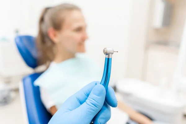 Close-up hand of dentist in the glove holds dental high speed turbine. The patient in blue chair at the background. Office where dentist conducts inspection and concludes. — Stock Photo, Image