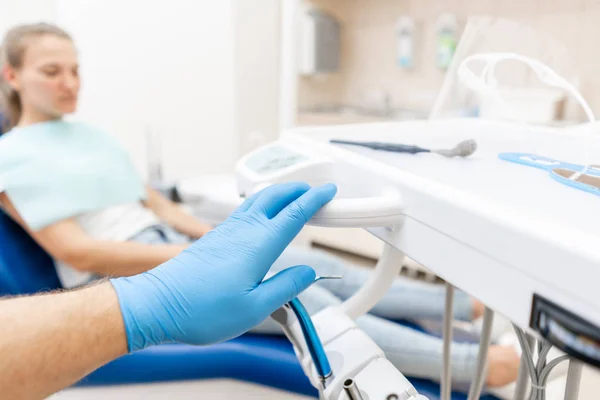 Κοντινό χέρι του οδοντίατρου στο γάντι κρατά οδοντοστρόβιλο υψηλής ταχύτητας. Ο ασθενής σε μπλε καρέκλα στο παρασκήνιο. Γραφείο όπου ο οδοντίατρος διεξάγει επιθεώρηση και. — Φωτογραφία Αρχείου