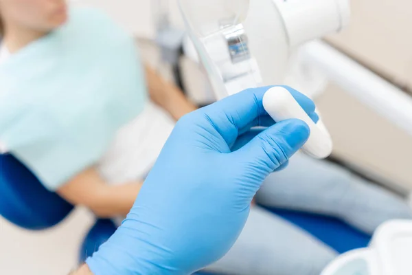 Κοντινό χέρι του οδοντίατρου στο γάντι ρυθμίζει τη λάμπα. Ο ασθενής σε μπλε καρέκλα στο παρασκήνιο. Γραφείο όπου ο οδοντίατρος διεξάγει επιθεώρηση και. — Φωτογραφία Αρχείου