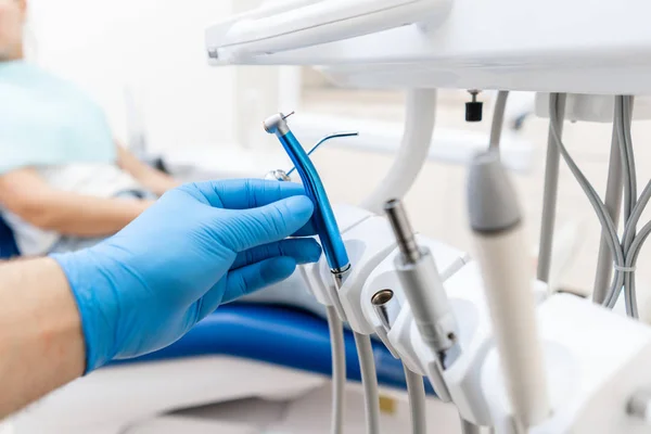 Close-up hand of dentist in the glove holds dental high speed turbine. The patient in blue chair at the background. Office where dentist conducts inspection and concludes. — Stock Photo, Image