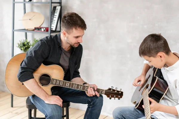 Il giovane padre guarda suo figlio imparare a suonare la chitarra. Educazione musicale familiare — Foto Stock