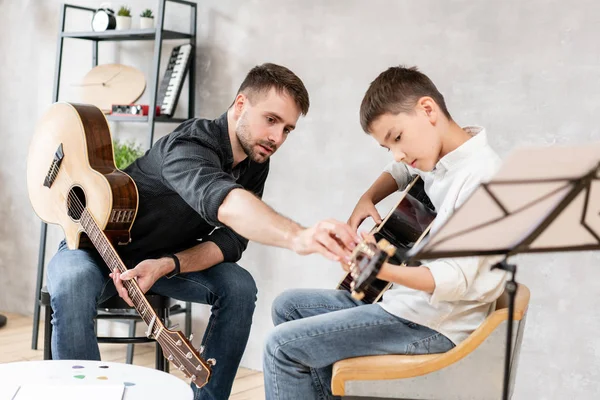 Yetişkin adam gitar çalmayı öğrenmek oğlu açıklar, nasıl doğru akor çalıştı çalmayı. Aile ile eğitim