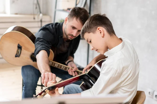 L'uomo adulto spiega a suo figlio, che impara a suonare la chitarra, come suonare correttamente gli accordi studiati. Istruzione con la famiglia — Foto Stock