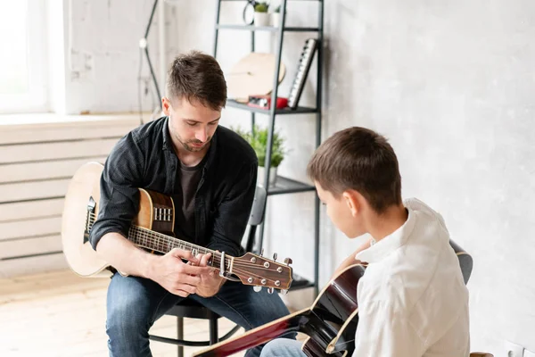 The young teacher shows the correct position of the hands in the guitar on his example — Stock Photo, Image