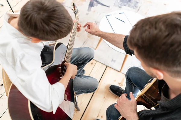 L'homme adulte explique à son fils, qui apprend à jouer de la guitare, comment jouer correctement de l'accord étudié. Éducation avec la famille — Photo