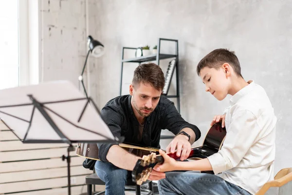 Hombre adulto explica a su hijo, que aprenden a tocar la guitarra, cómo tocar el acorde estudiado correctamente. Educación con la familia — Foto de Stock