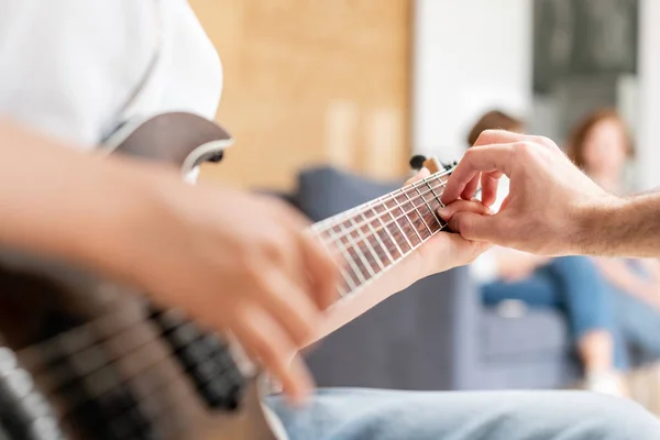 Giovane ragazzo muove la mano lungo le corde della chitarra mentre suo padre aiuta il ragazzo a prendere accordi — Foto Stock