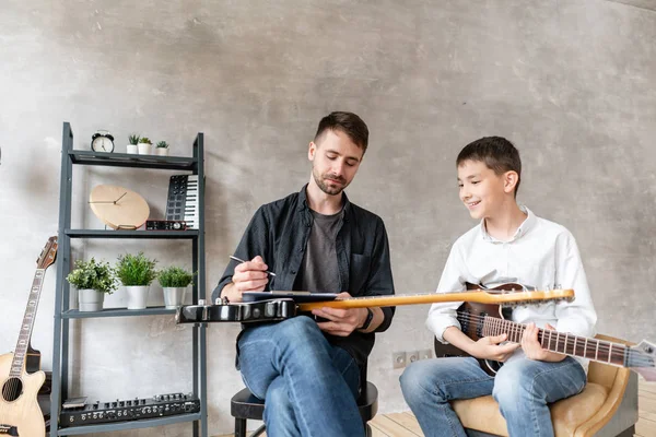 Küçük öğrenci müzik notaları üzerine notlar yazıyor onun müzik öğretmeni saatler