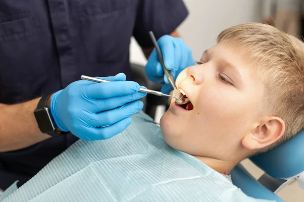 Un giovane ragazzo è sdraiato sulla sedia dentale e viene esaminato da un medico — Foto Stock