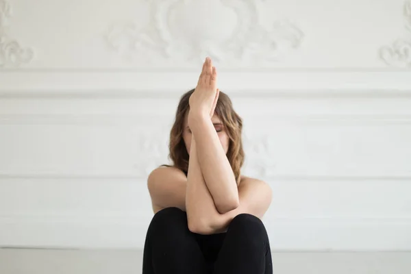 Kvinna i en träningsoverall sitter mot väggen håller händerna framför hennes ansikte — Stockfoto