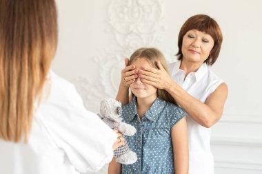 Adult woman closes her daughter eyes while her older daughter prepare gift for younger one. Selective focus