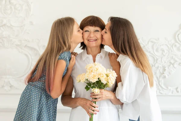 Grandmother holding flowers in hands, her daughter and granddaughter hug each other and smile