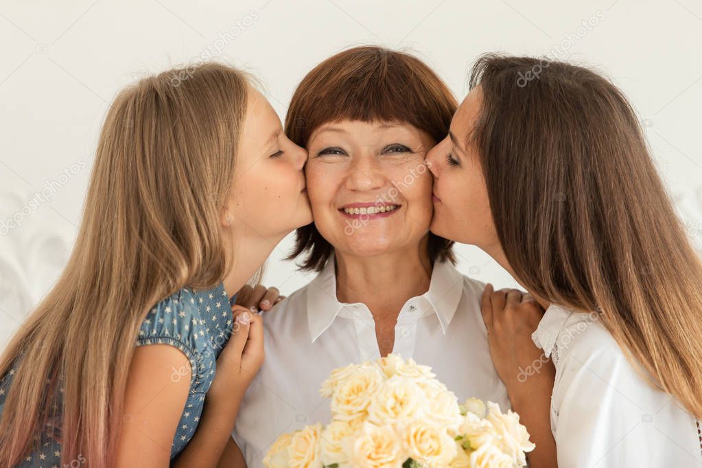 Grandmother holding flowers in hands, her daughter and granddaughter hug each other and smile