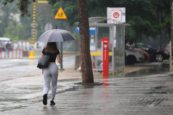 Sokakta yağmurun altında şemsiyeli bir kadın.
