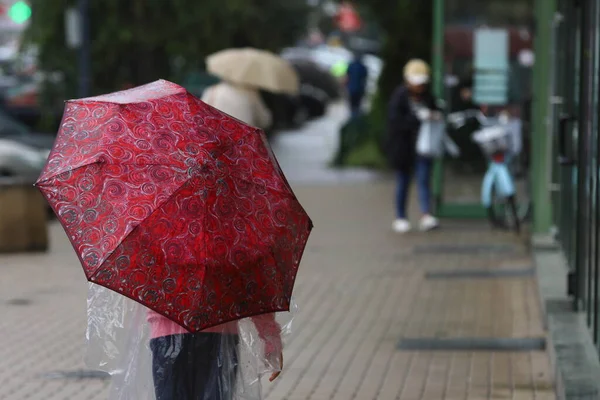 Sokakta yağmurun altında kırmızı şemsiyeli küçük kız