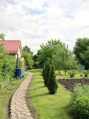Güneşli bir günde yeşil ağaçlar ve çalılarla çevrili bir arazide, fotokopi alanı olan dikey formatta bir eve giden yol.
