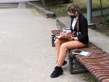 Takım elbiseli genç bir kadın ıssız bir bankta oturuyor. Tabletteki kulaklıklardan bir şeyler dinliyor ve not defterine not alıyor. Kopya alanı ile karantina sırasında uzak çalışma veya eğitim