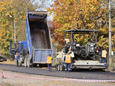 Pestovo, Veliky Novgorod, Rusya - 28 Eylül 2020: Birçok sarı yaprağın ağaçlardan düştüğü bir sonbahar günü yeni asfalt yapmak için kaldırılmış ceset, asfalt kaldırıcı ve çalışma ekibi